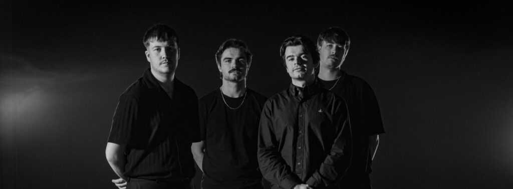 Four men stood together looking at the camera, the image is in black and white.