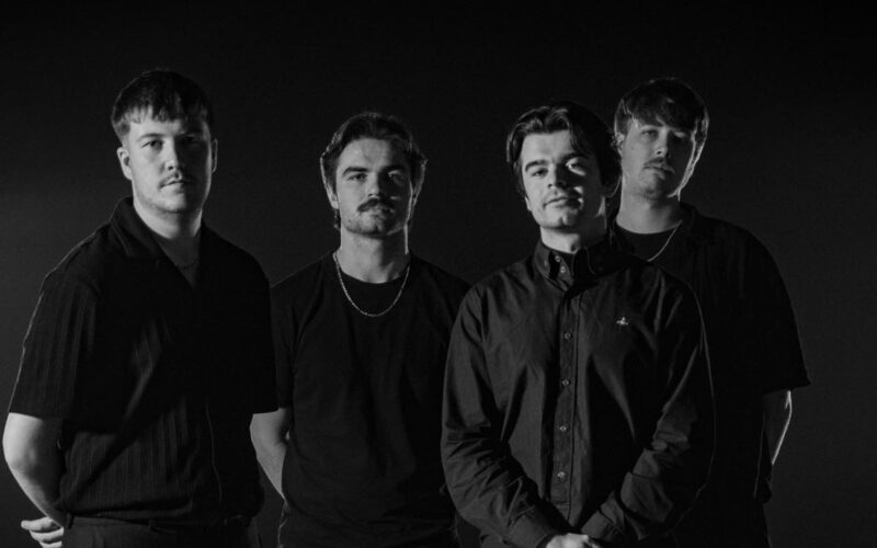 Four men stood together looking at the camera, the image is in black and white.